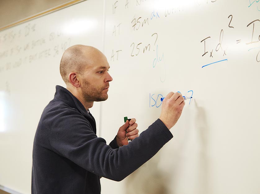 A professor writes a Chemistry equation on a whiteboard.
