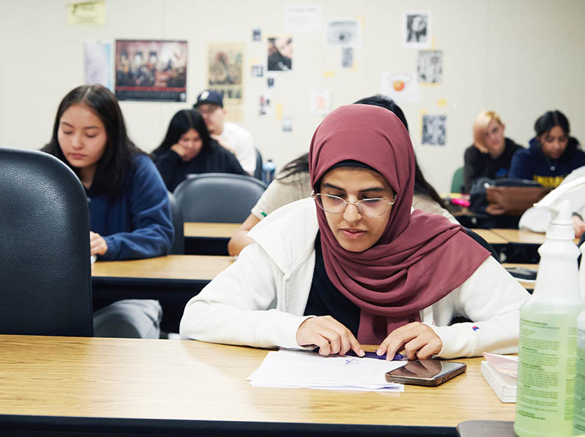 Classroom of students reviewing their papers, with female student in foreground with head scarf.