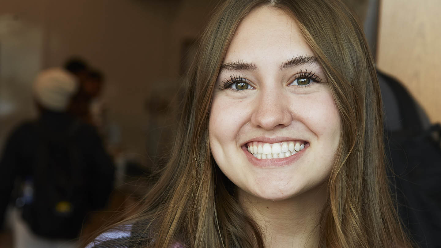 Young female graduate in plaid shirt has bright eyes and wide grin.