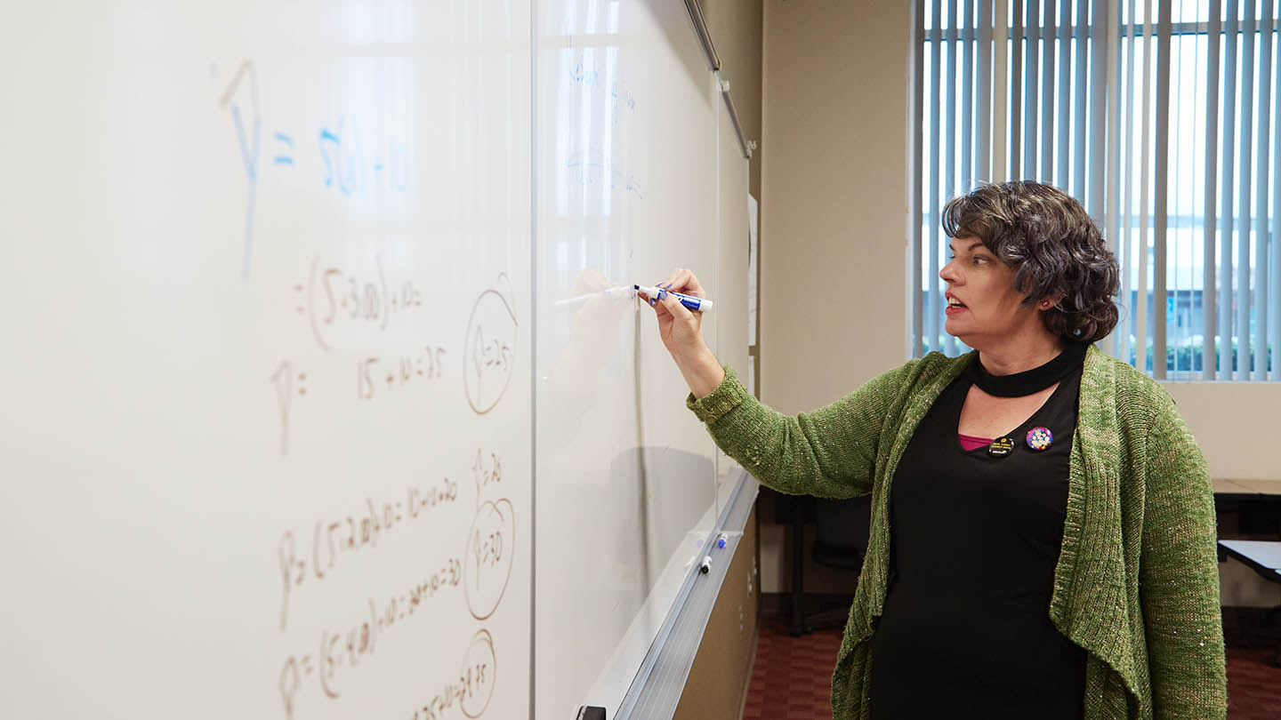 A professor writes on a whiteboard to help students understand a difficult concept.
