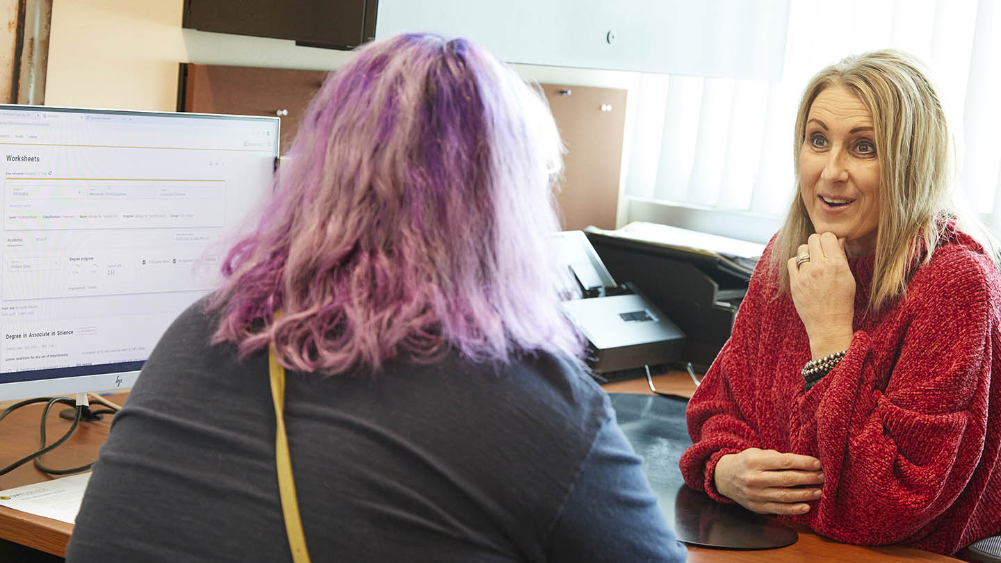 A smiling counselor speaks to a student across a desk in the Student Services department.