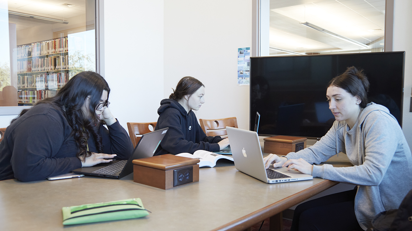 Three female students work collaboratively in one of the library private study rooms.