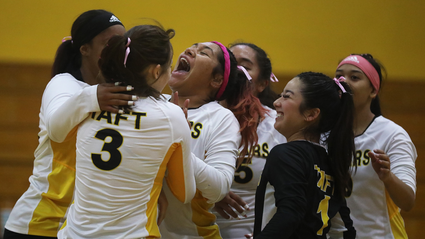Six female Taft College teammates in uniforms gather for a group hug and, the central student shouts for joy.