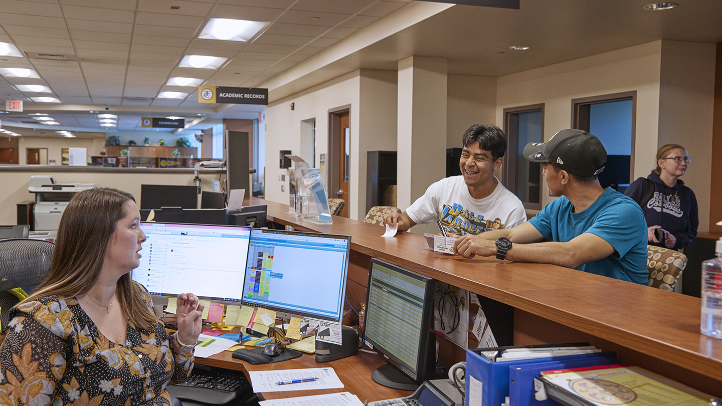 A female staff member helps provide some clarity to two student athletes.