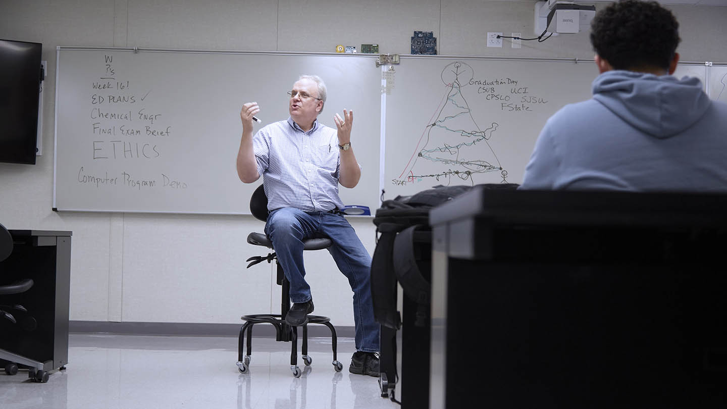 Male professor in front of blackboard talks to Engineering class.