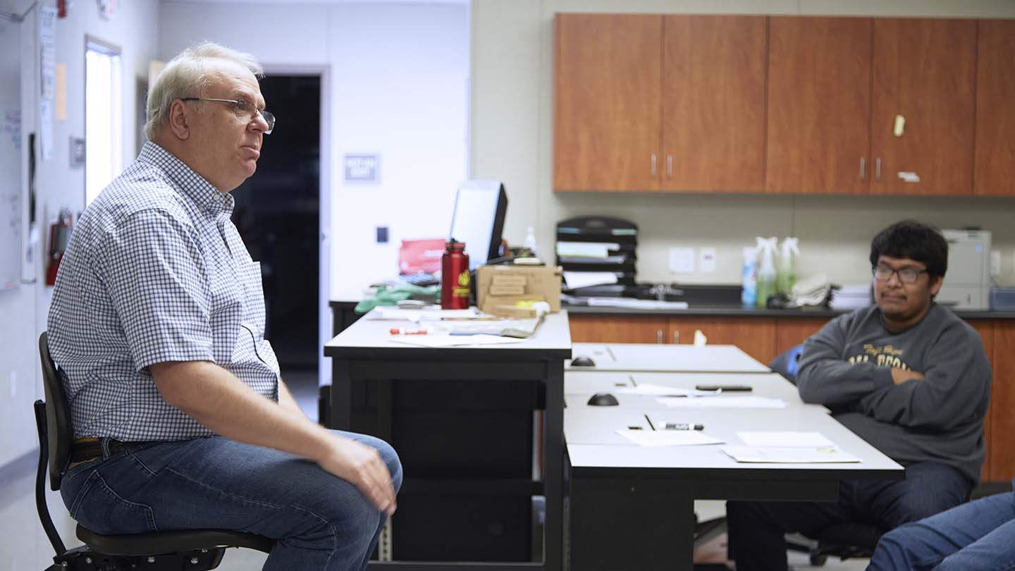 Professor at head of the class is captivated as he listens to a student's response.