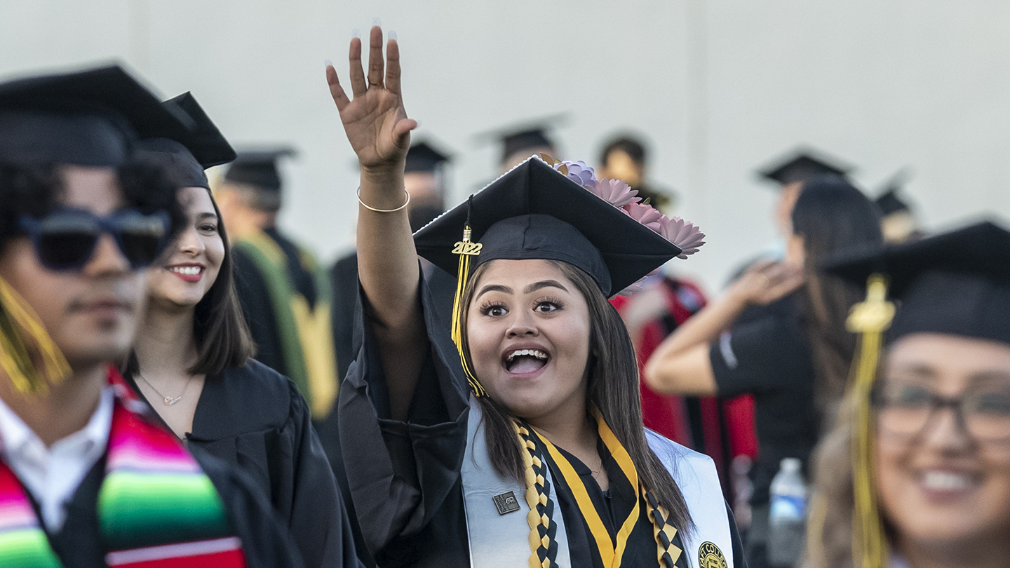 Class of 2022 enters stadium as commencement begins and female graduate waves to her family.