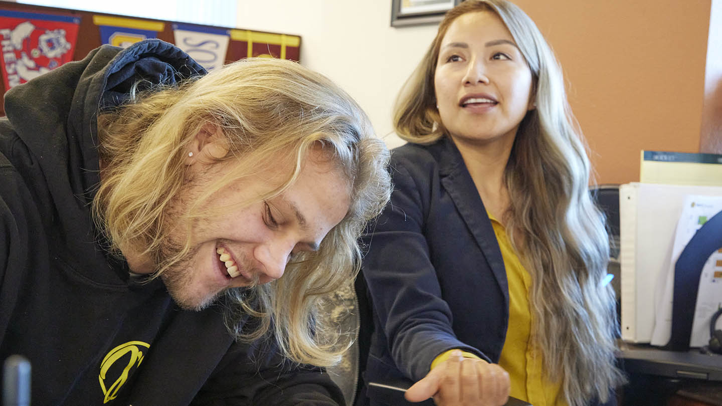 Male student leans in to fill out a form as a female technician holds out her hand awaiting the document.