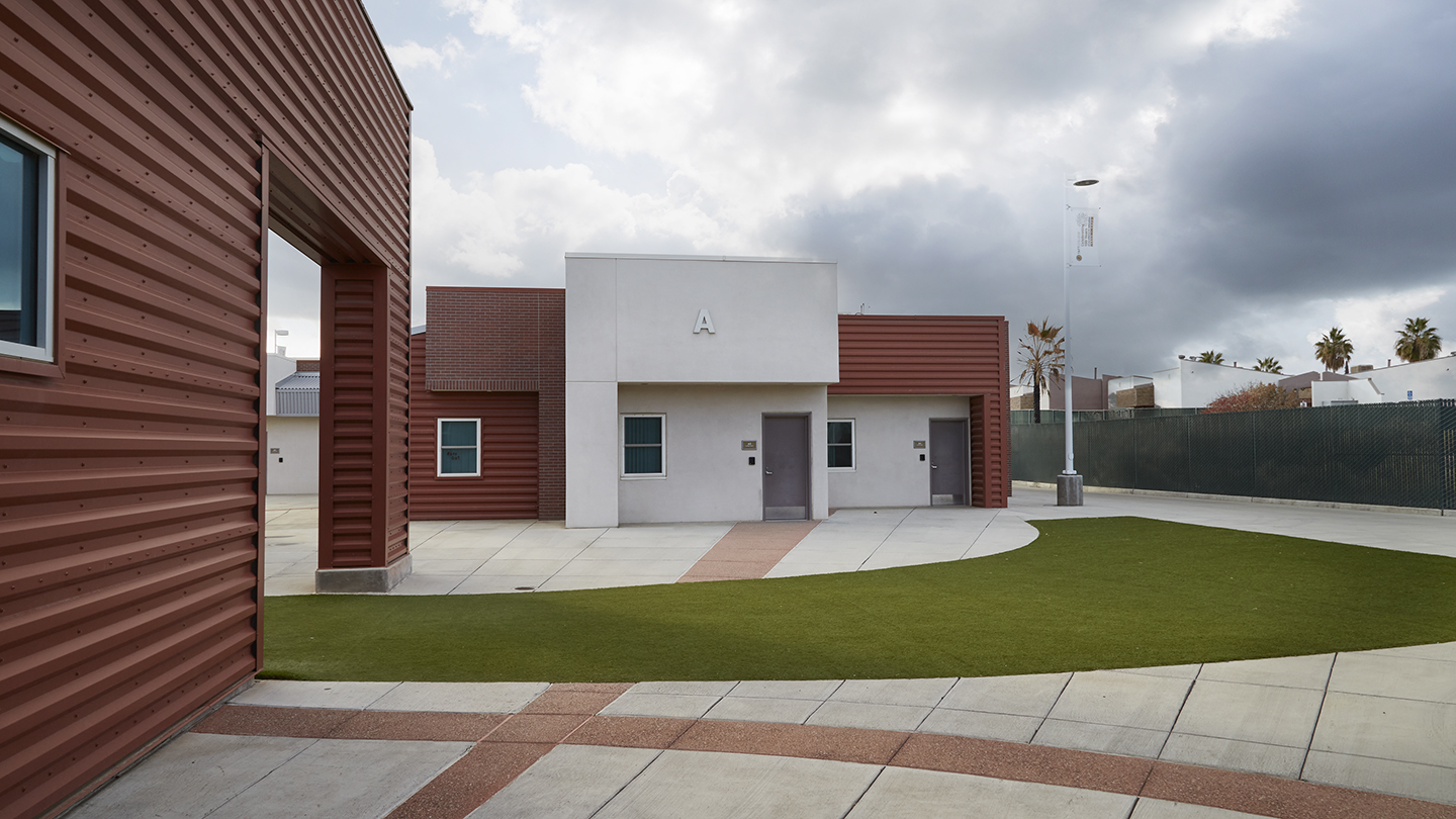 Stylish one-story building in colors of white and brick red has an interesting angular design with front projections that complements and contrasts with the design of the patio grid and curved swath of green grass in front. It has two outside entrance doors.